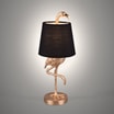 Lampa stołowa w kształcie złotego flaminga z czarnym otaczającym go abażurem zaświecona, na szarym tle widoczna od przodu.