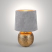 Lampa stołowa z abażurem popielato-złota zaświecona, widoczna od przodu.
