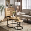 Dwa okrągłe stoliki kawowe na dywanie z roślinnym wzorem. W tle widoczna sofa, komoda i lampa podłogowa.