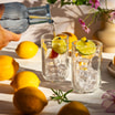Woda nalewana z karafki do szklanek z kostkami lodu i plasterkami limonki, ustawionych wśród cytryn i kwiatów.