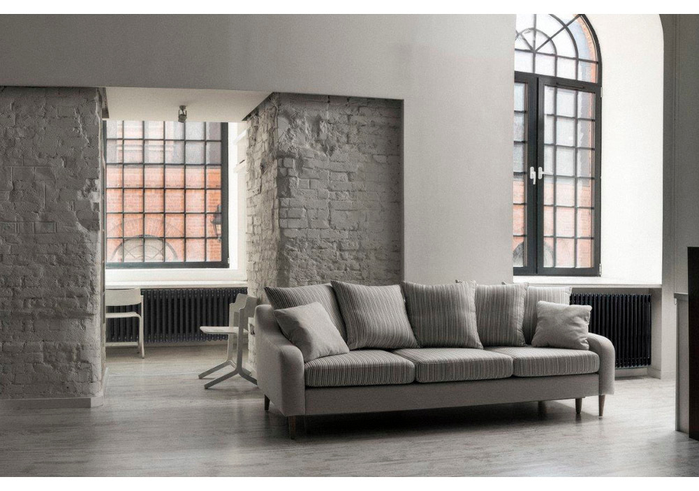Szara sofa trzyosobowa w loftowym salonie z ceglaną ścianą i dużymi industrialnymi oknami