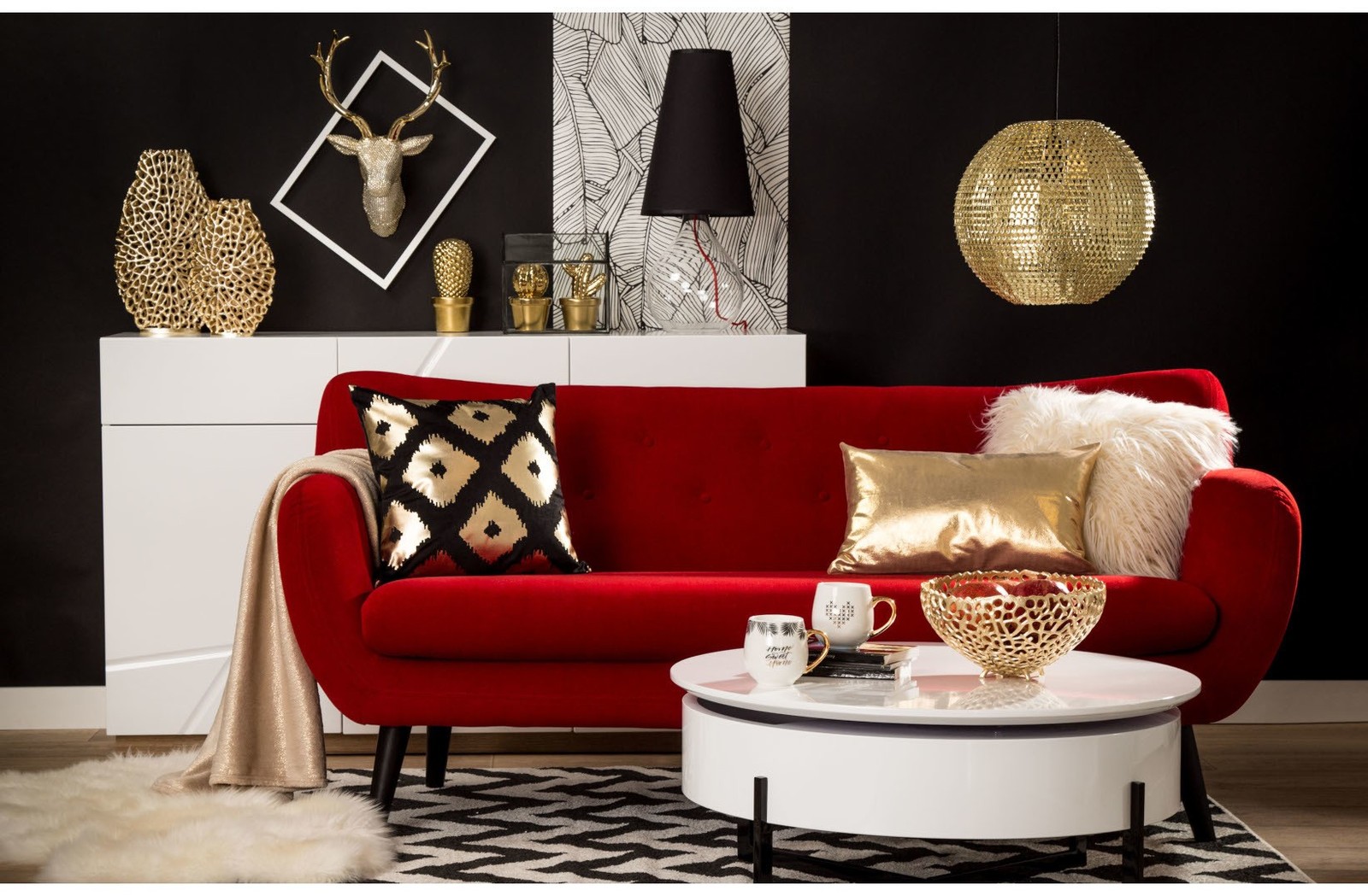 Czerwona sofa w stylu glamour z białym stolikiem kawowym oraz złotymi dekoracjami, prezentowana w eleganckim salonie z czarną ścianą i designerskim oświetleniem.