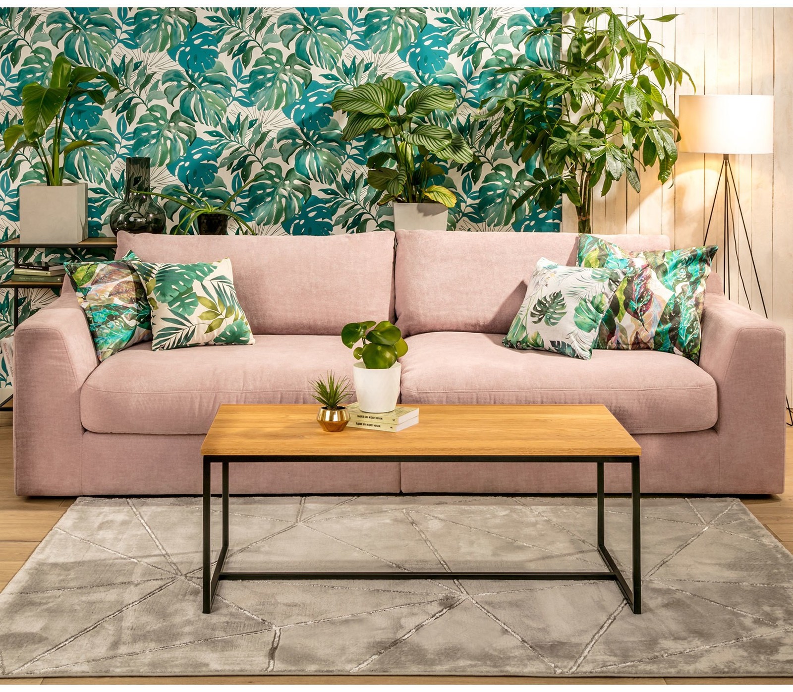 Jasnoróżowa sofa z poduszkami w tropikalne liście w salonie urządzonym w modnym stylu urban jungle.