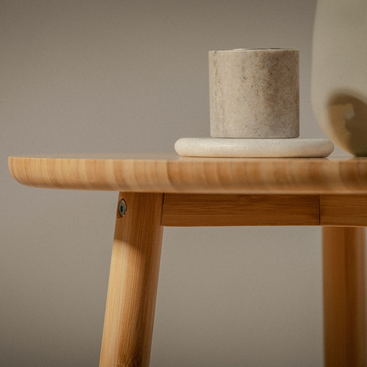 Zbliżenie na drewniany stolik pomocniczy z okrągłym blatem, nowoczesny mebel do salonu lub sypialni z ceramiczną świecą w minimalistycznej aranżacji wnętrza.