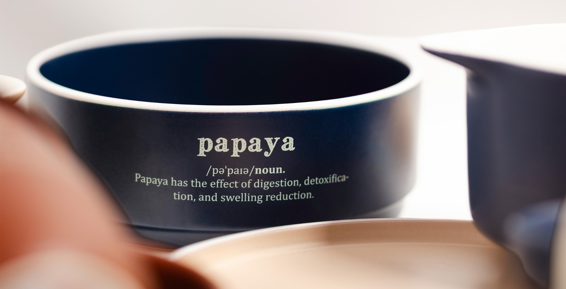 Zbliżenie na granatową miskę z dekoracyjnym napisem papaya. W tle widoczne elementy zastawy.