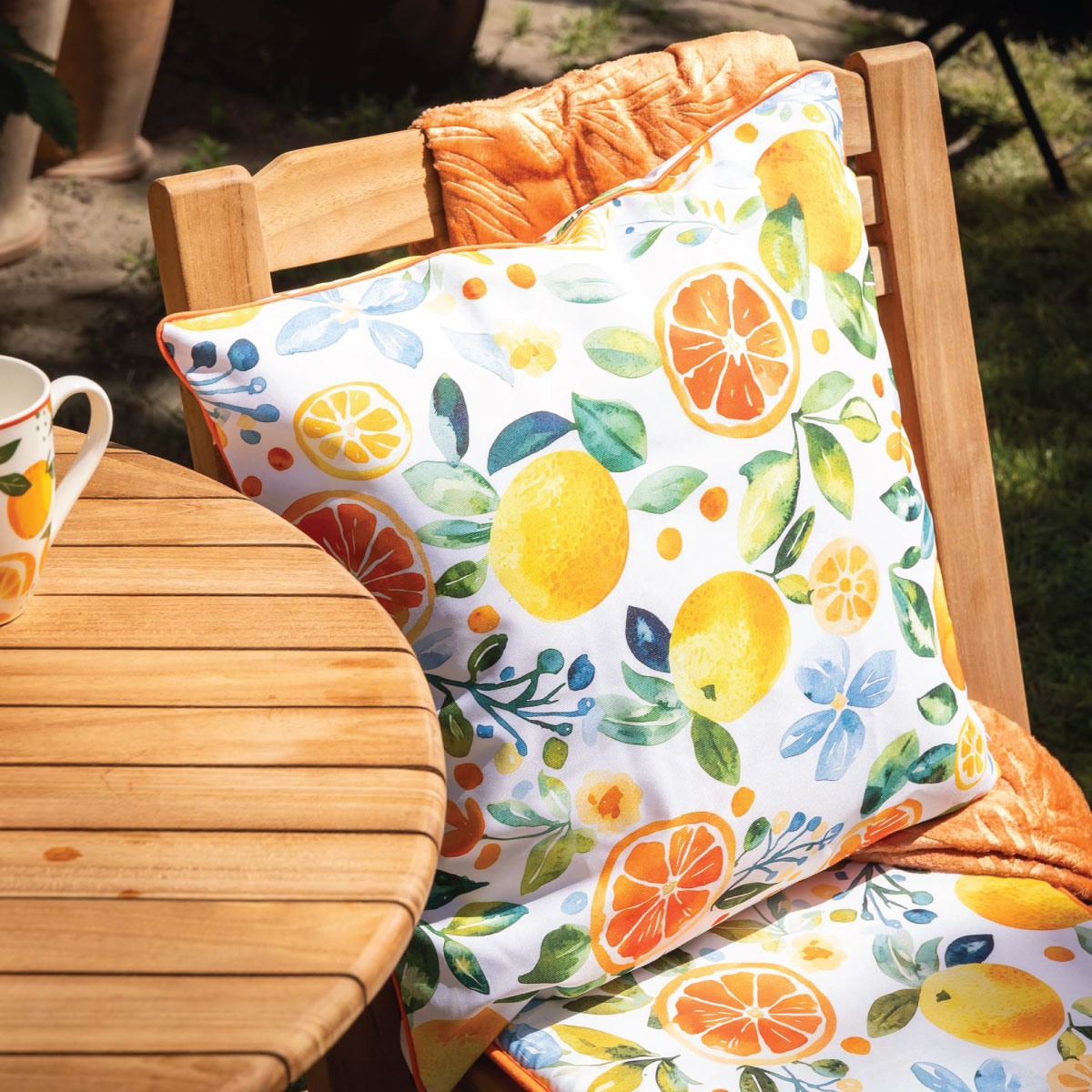 Zbliżenie na poduszkę SUN&CITRUS z kolorowym wzorem pomarańczy i liści.