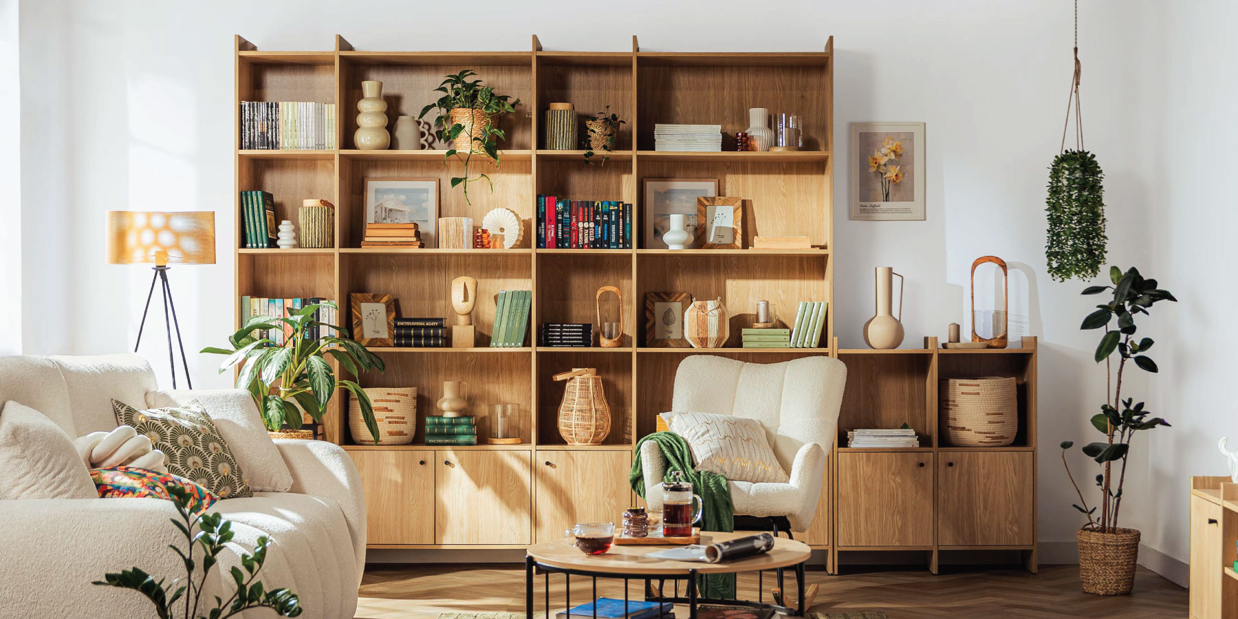 Salon w stylu Retro z modułową zabudową ściany z regałów kolekcji Magnus, z jasną sofą Soro, fotelem bujanym Jexla, roślinami oraz dekoracjami.