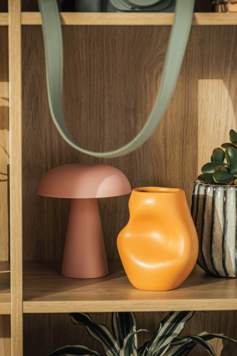 Różowa lampa stołowa oraz ceramiczny żółty wazon ustawione na półce regału Magnus.