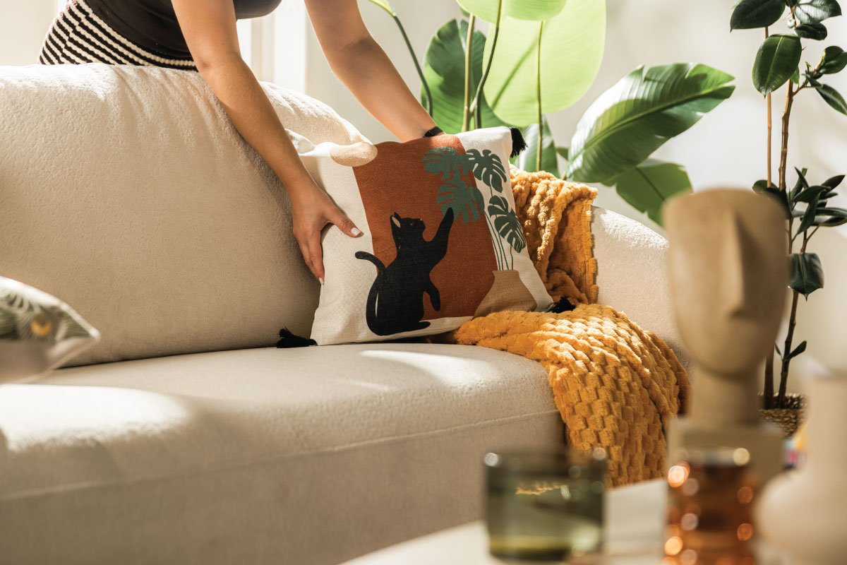 Beżowa sofa Roma z dekoracyjną poduszką z graficznym czarnym kotem CATS oraz musztardowym kocem w przytulnym salonie w stylu etno.