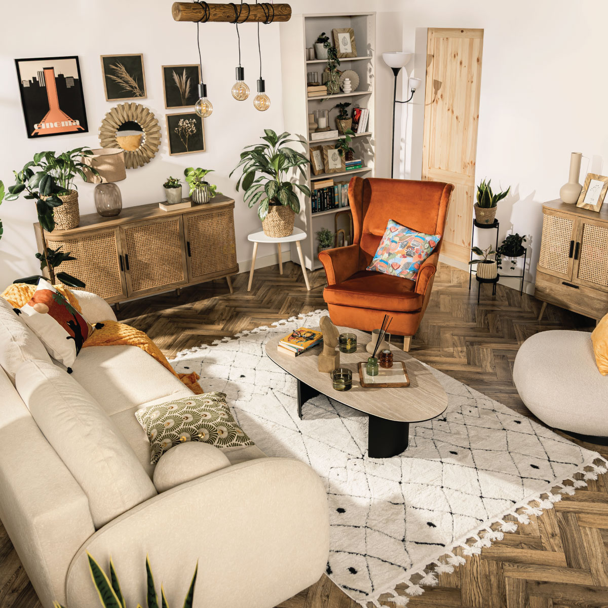 Przytulny salon w stylu etno z sofą Roma, ceramiczną ławą Remdovia, pomarańczowym fotelem typu uszak Maivilli, kremowym obotowym fotelem Vizzo, meblami z kolekcji Fabla oraz regałem w kolorze kaszmir Alice Springs.