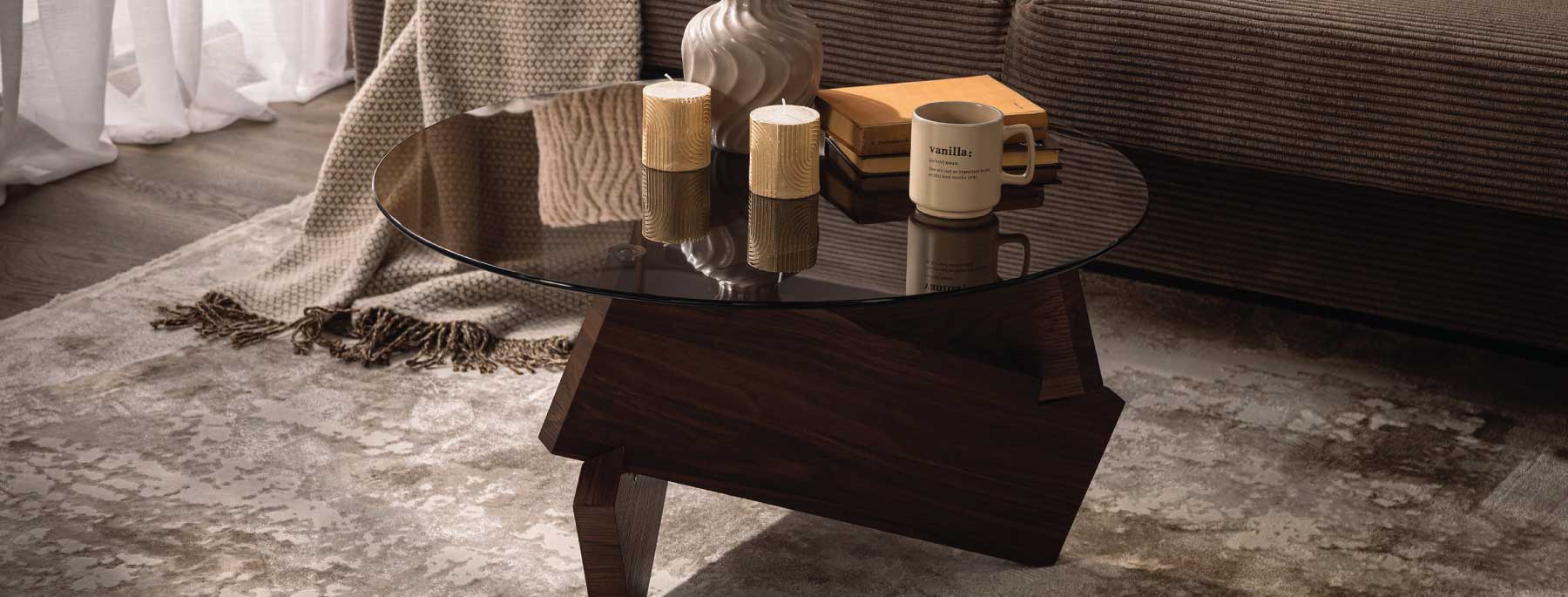 Brązowy stolik kawowy Lecerril przed wersalką Sonia z świecami i dekoracją z suszonych traw.