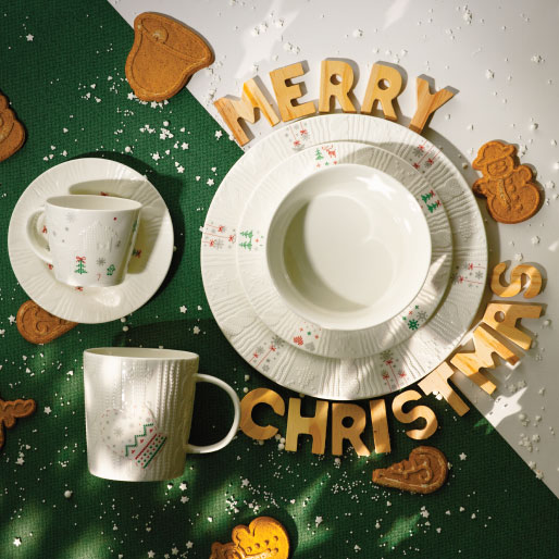 Świąteczna kompozycja z porcelanowymi talerzami, filiżankami i kubkiem ułożonymi na zielonym tle z napisem Merry Christmas.