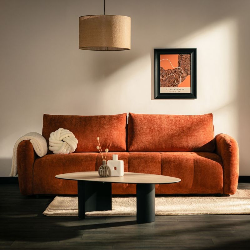 Rdzawobrązowa sofa do salonu z miękkim tapicerowanym siedziskiem, ustawiona przy nowoczesnym stoliku kawowym w eleganckiej aranżacji wnętrza z ciepłymi akcentami kolorystycznymi.