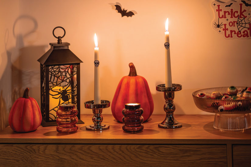 Dekoracje Halloween na komodzie: dynie, latarnia, świeczniki z zapalonymi świecami i patera