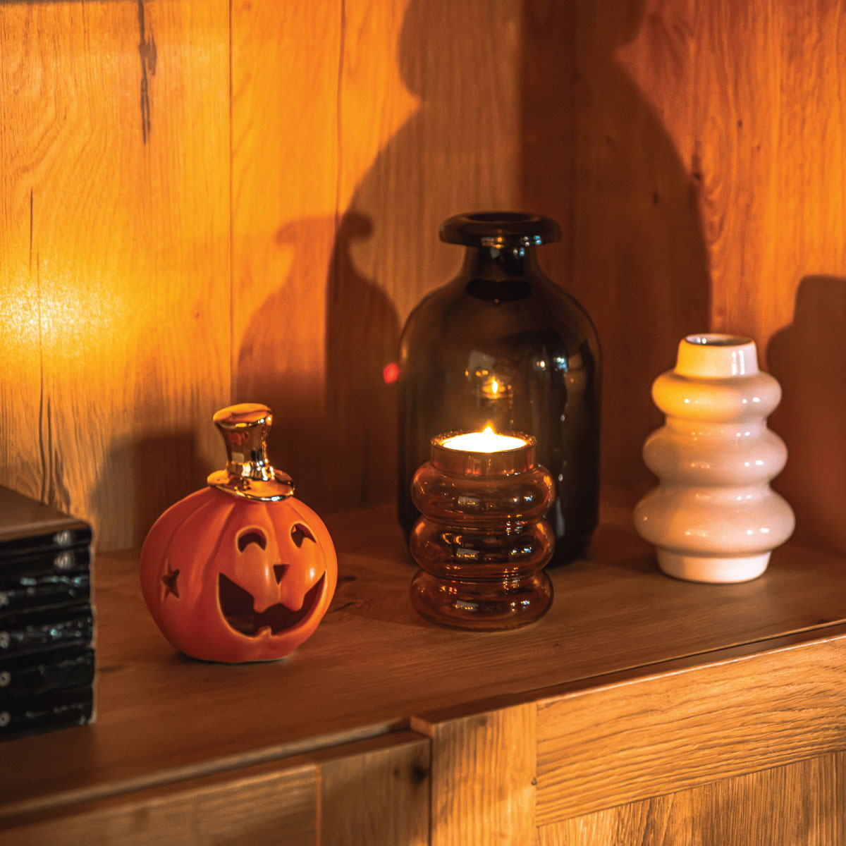 Regał z dekoracjami Halloween: figurka dyni, czarny i biały wazon oraz książki
