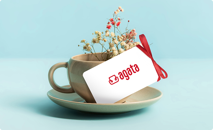 Karta podarunkowa Agata przewiązana czerwoną wstążką w filiżance z kwiatami.