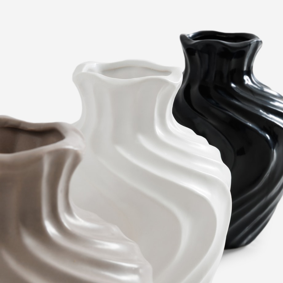 Trzy ceramiczne wazony o falistej formie ustawione obok siebie w beżu, bieli i czerni.
