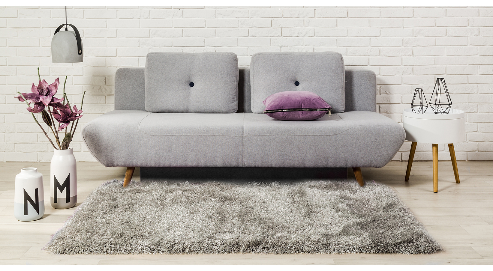 Szara sofa rozkładana na dywanie o wysokim runie