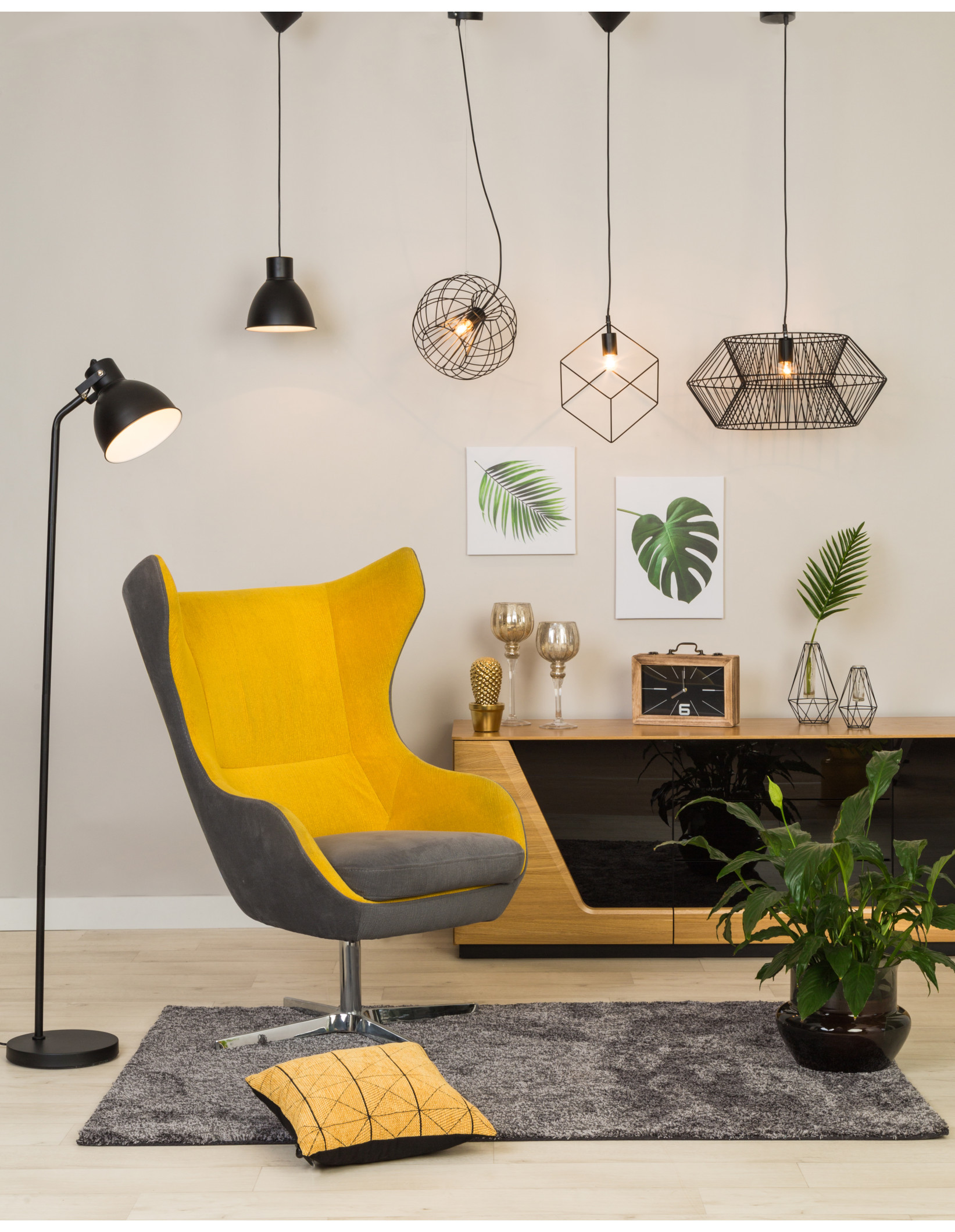 Żółto-szary fotel uszak w nowoczesnym salonie, z designerskimi lampami wiszącymi, drewnianą szafką RTV, dekoracjami ściennymi i roślinami w stylu loftowym oraz skandynawskim.