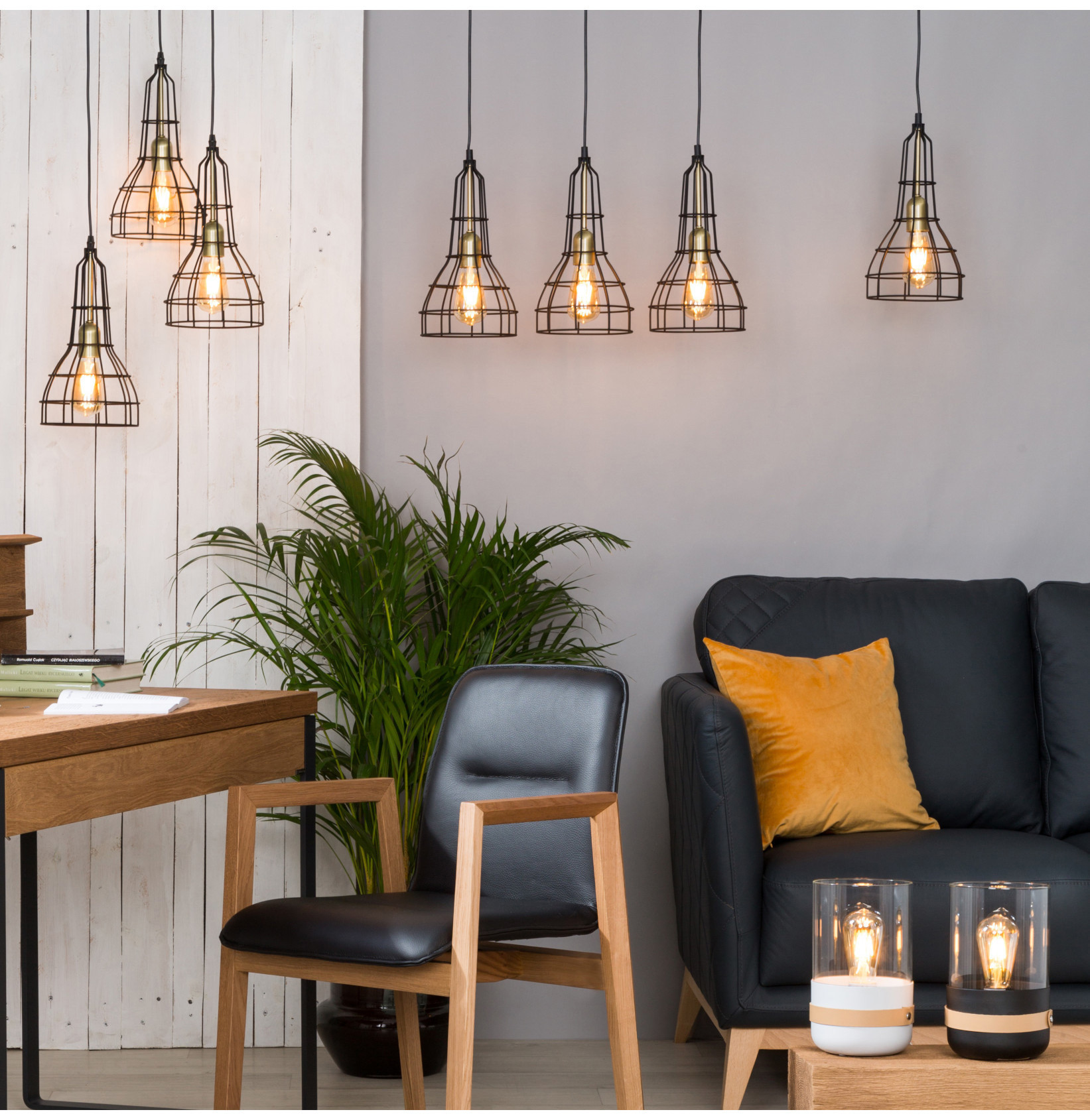 Loftowe lampy wiszące z żarówkami Edison w nowoczesnym wnętrzu z drewnianymi meblami i roślinami.