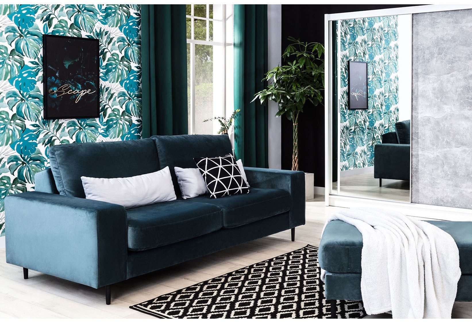 Granatowa sofa welurowa w stylu glamour, ustawiona w nowoczesnym salonie z tropikalną tapetą, szafą przesuwną z lustrem oraz dodatkami w stylu urban jungle.