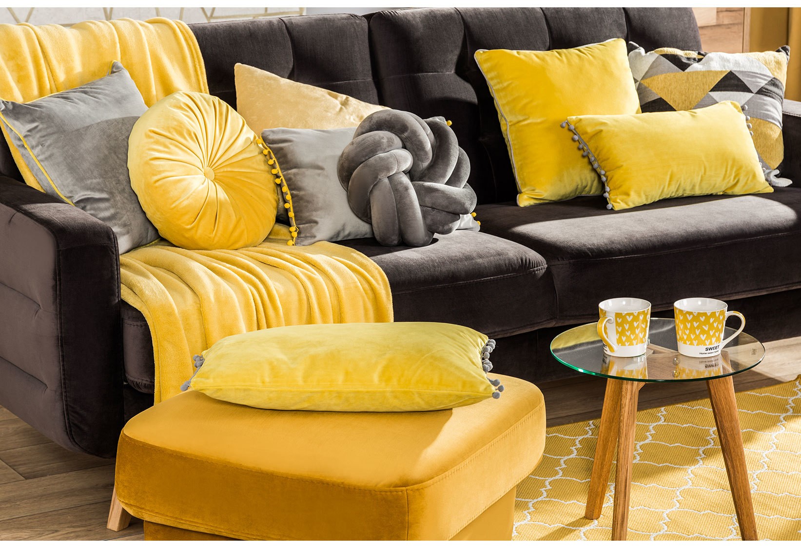 Szara sofa z żółtymi poduszkami i pufą