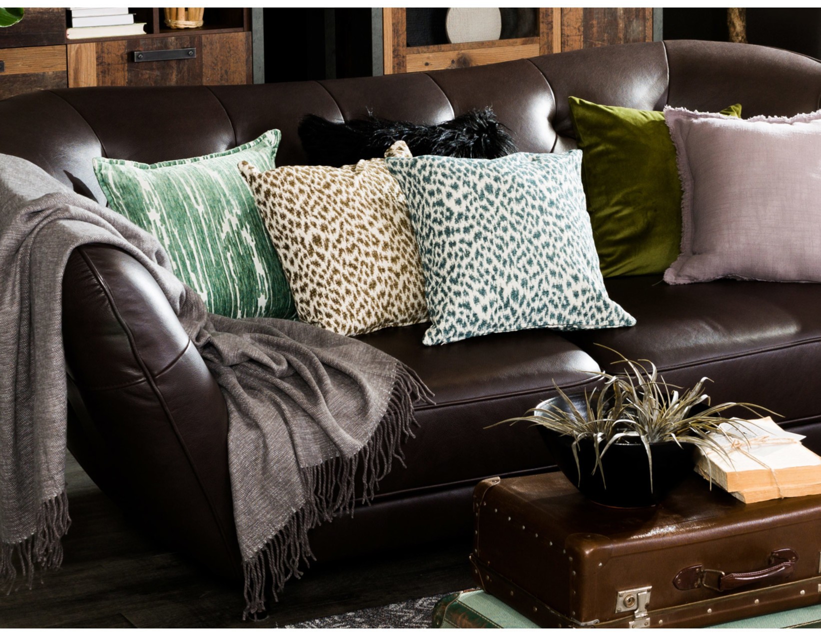 Brązowa sofa skórzana z kolorowymi poduszkami i kocem.