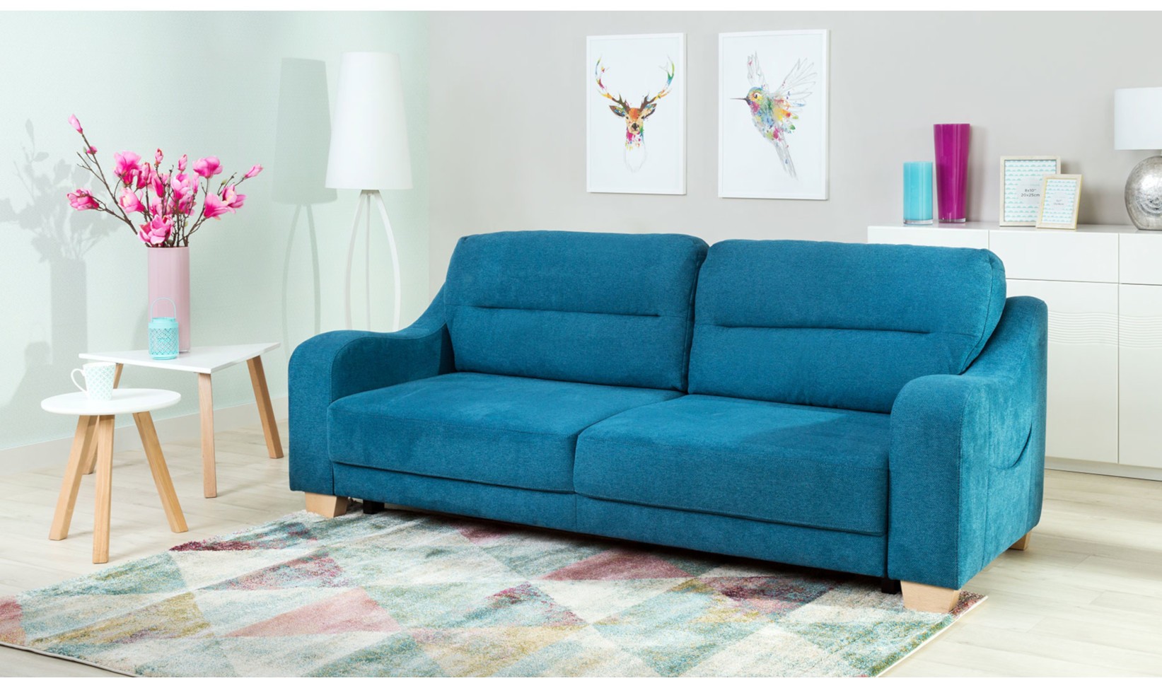 Turkusowa sofa na kolorowym dywanie w jasnym pokoju.