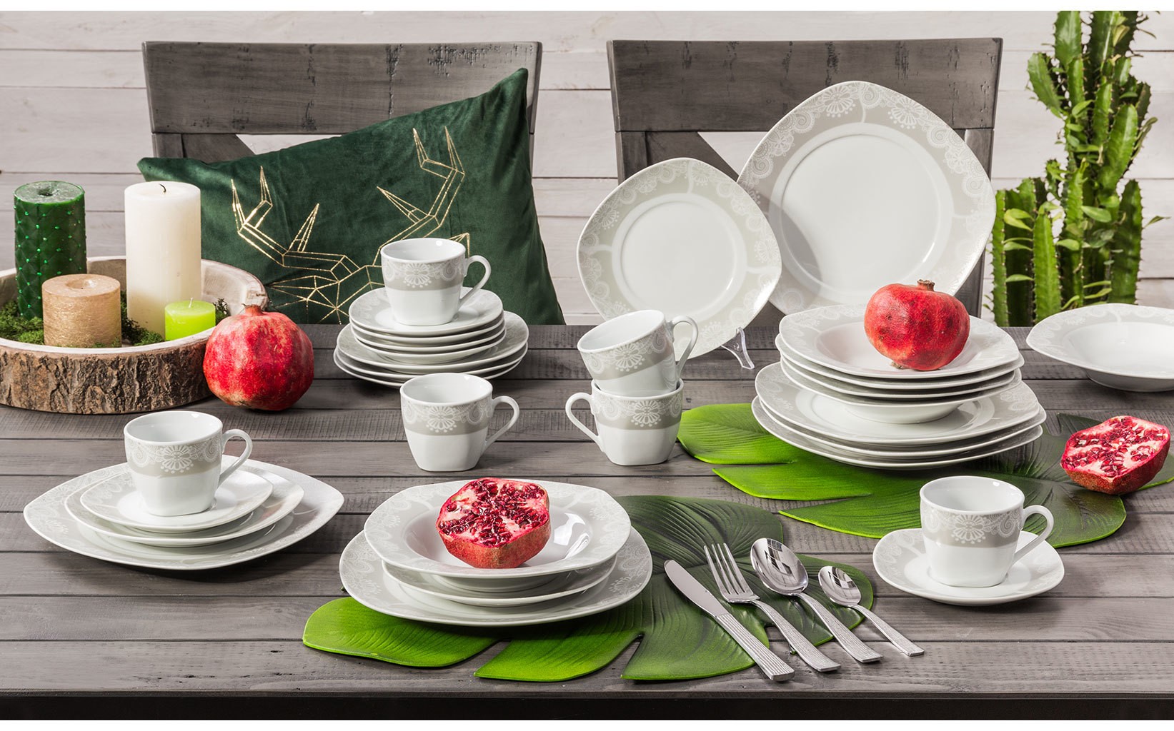 Elegancki serwis obiadowy z porcelanowymi talerzami i filiżankami w jasnym kolorze, ustawiony na drewnianym stole z dekoracyjnymi dodatkami i owocami.