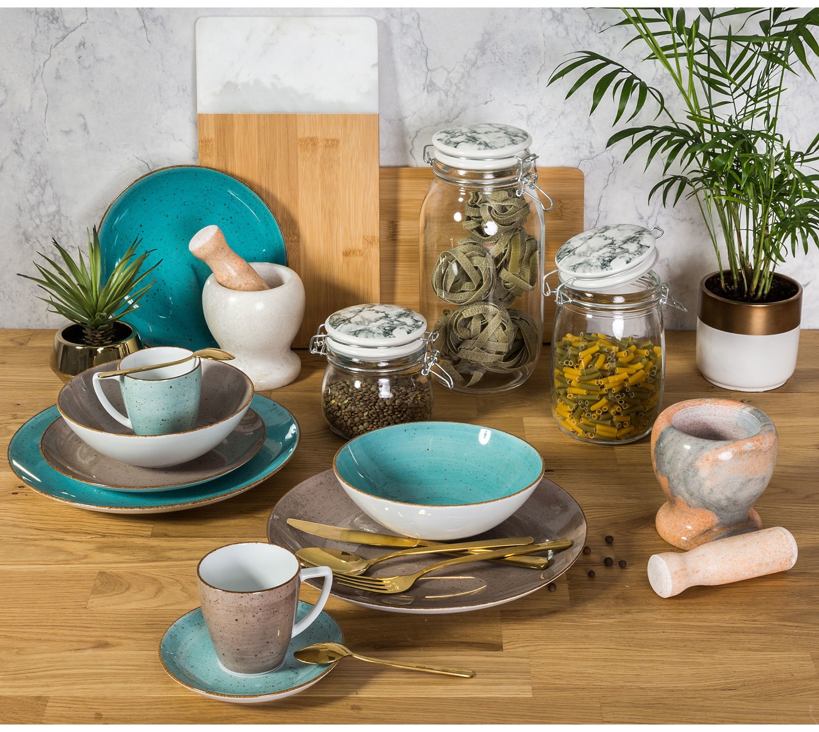 Nowoczesna zastawa ceramiczna w stylu loftowym z turkusowymi talerzami, kubkami i złotymi sztućcami, wyeksponowana na drewnianym blacie kuchennym z dekoracyjnymi słoikami.