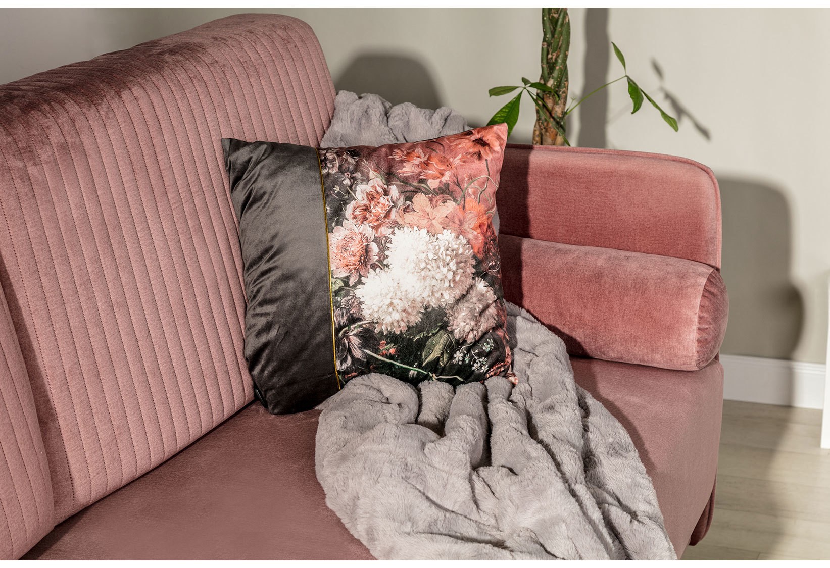 Różowa sofa welurowa w stylu glamour z dekoracyjną poduszką w kwiatowy wzór i miękkim futrzanym kocem, prezentowana w eleganckiej aranżacji nowoczesnego salonu.