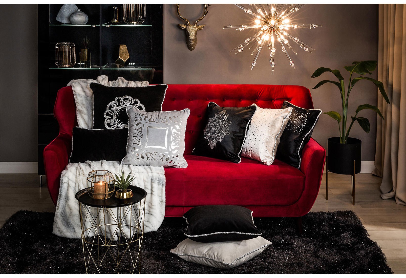 Salon w stylu glamour z czerwoną welurową sofą, srebrnymi dodatkami, dekoracyjnymi poduszkami i designerską lampą sufitową.