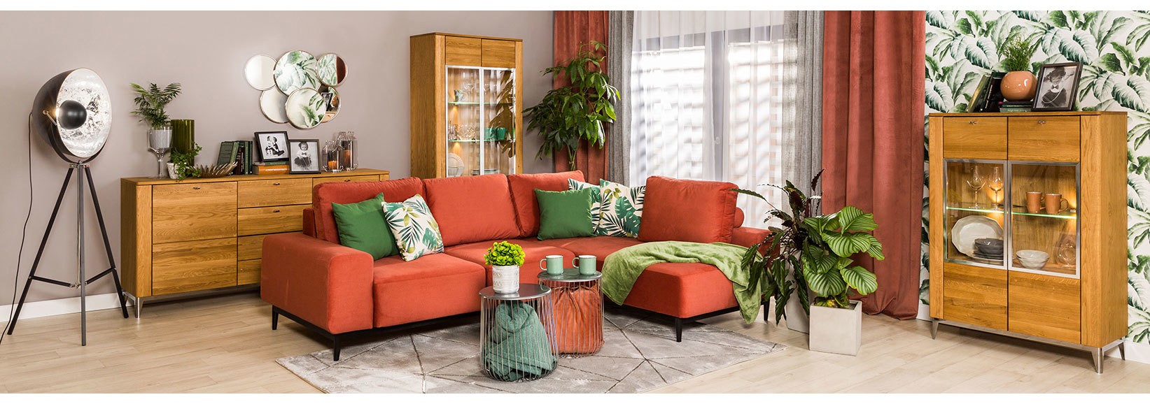 Pomarańczowa sofa w salonie z drewnianymi meblami, zielonymi dodatkami i roślinną tapetą
