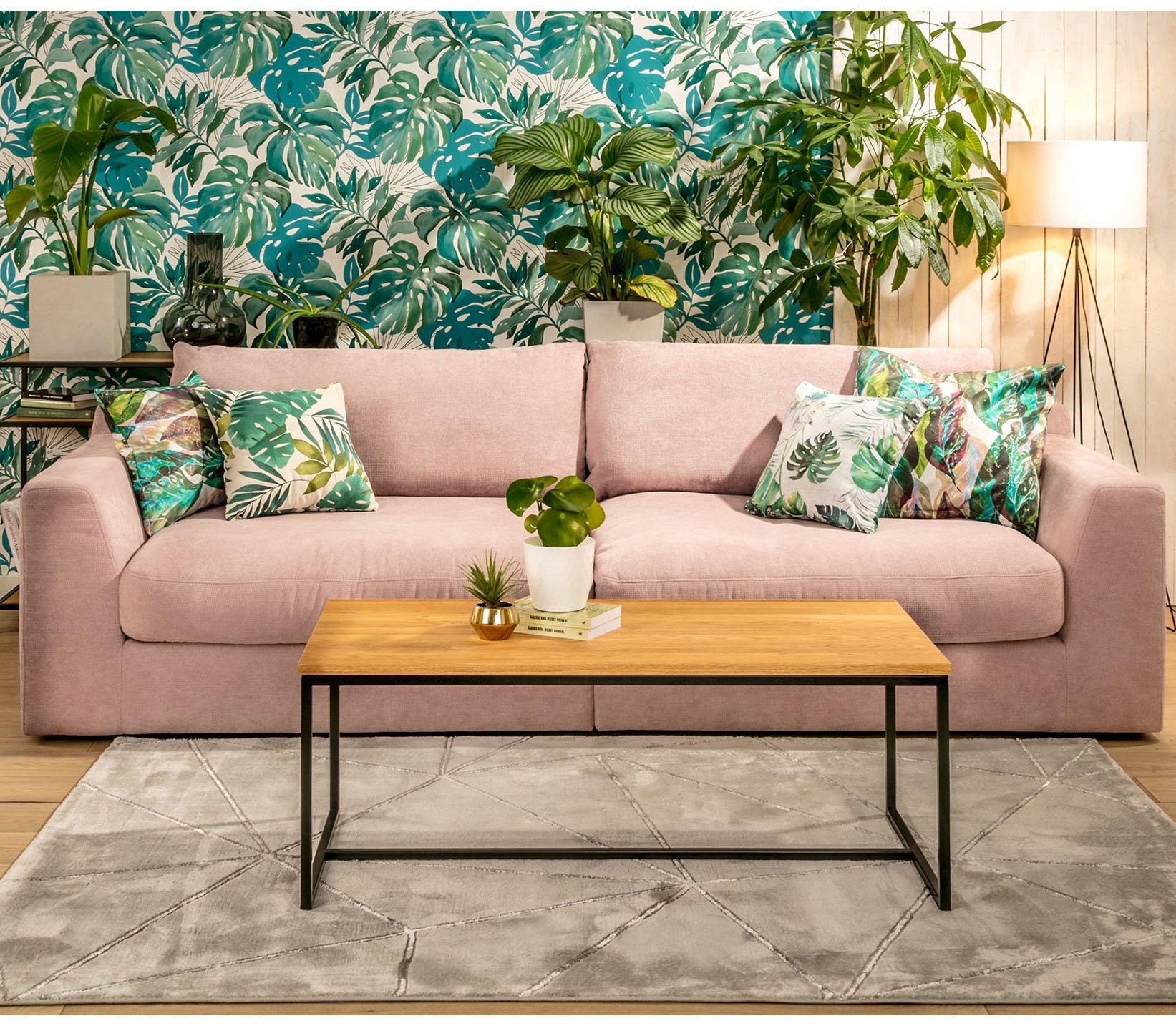 Jasnoróżowa sofa z poduszkami w tropikalne liście w salonie urządzonym w modnym stylu urban jungle.