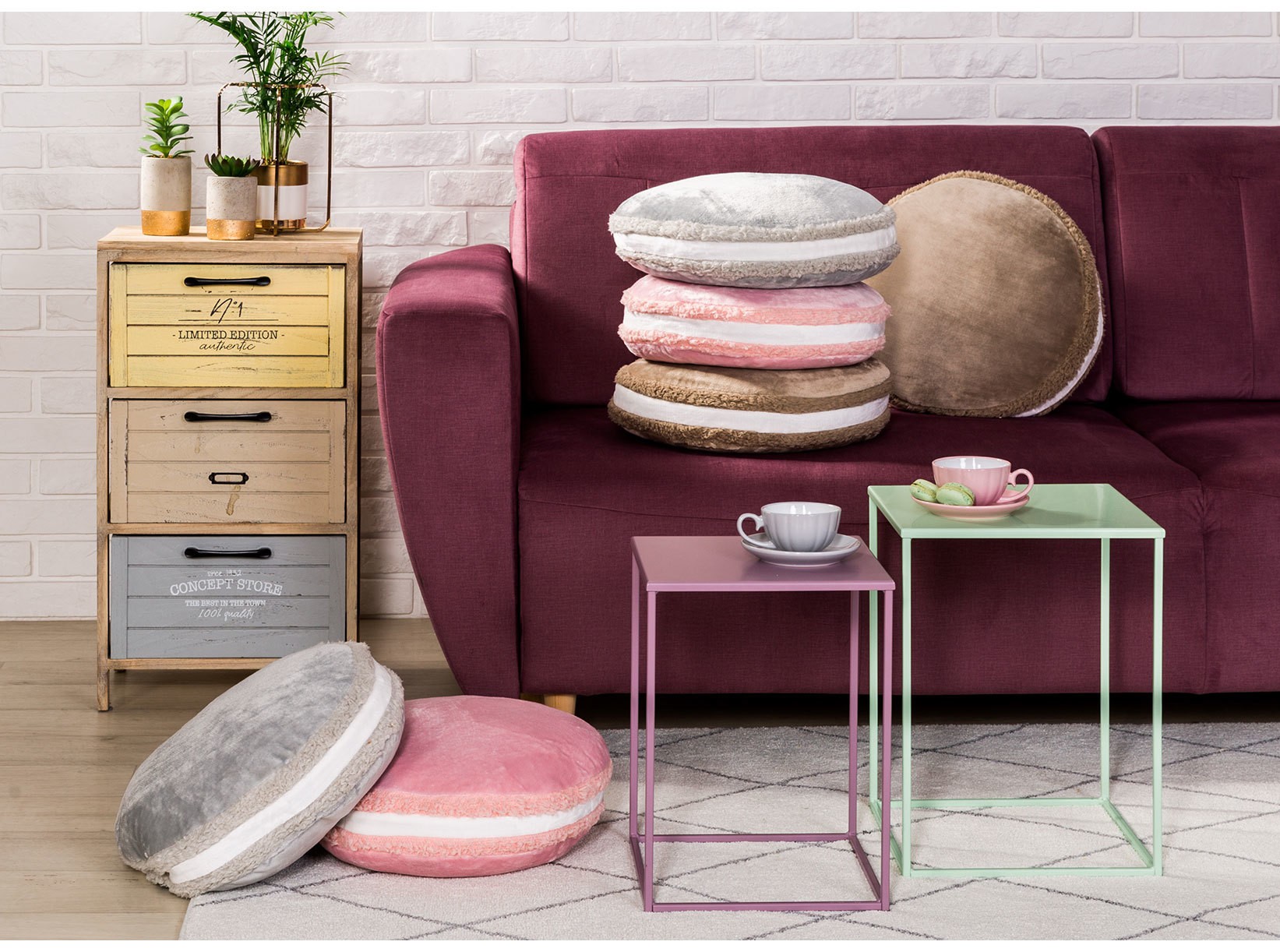 Bordowa sofa z okrągłymi poduszkami i metalowymi stolikami.