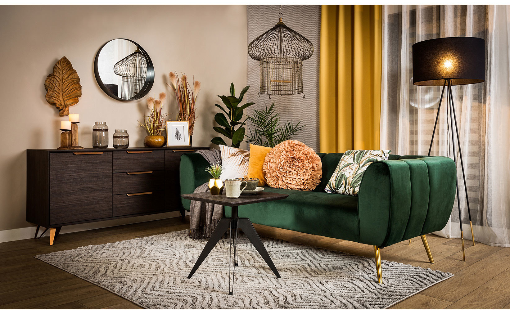 Zielona aksamitna sofa ze złotymi nóżkami, ciemna komoda i musztardowe zasłony w eleganckim salonie modern glamour.