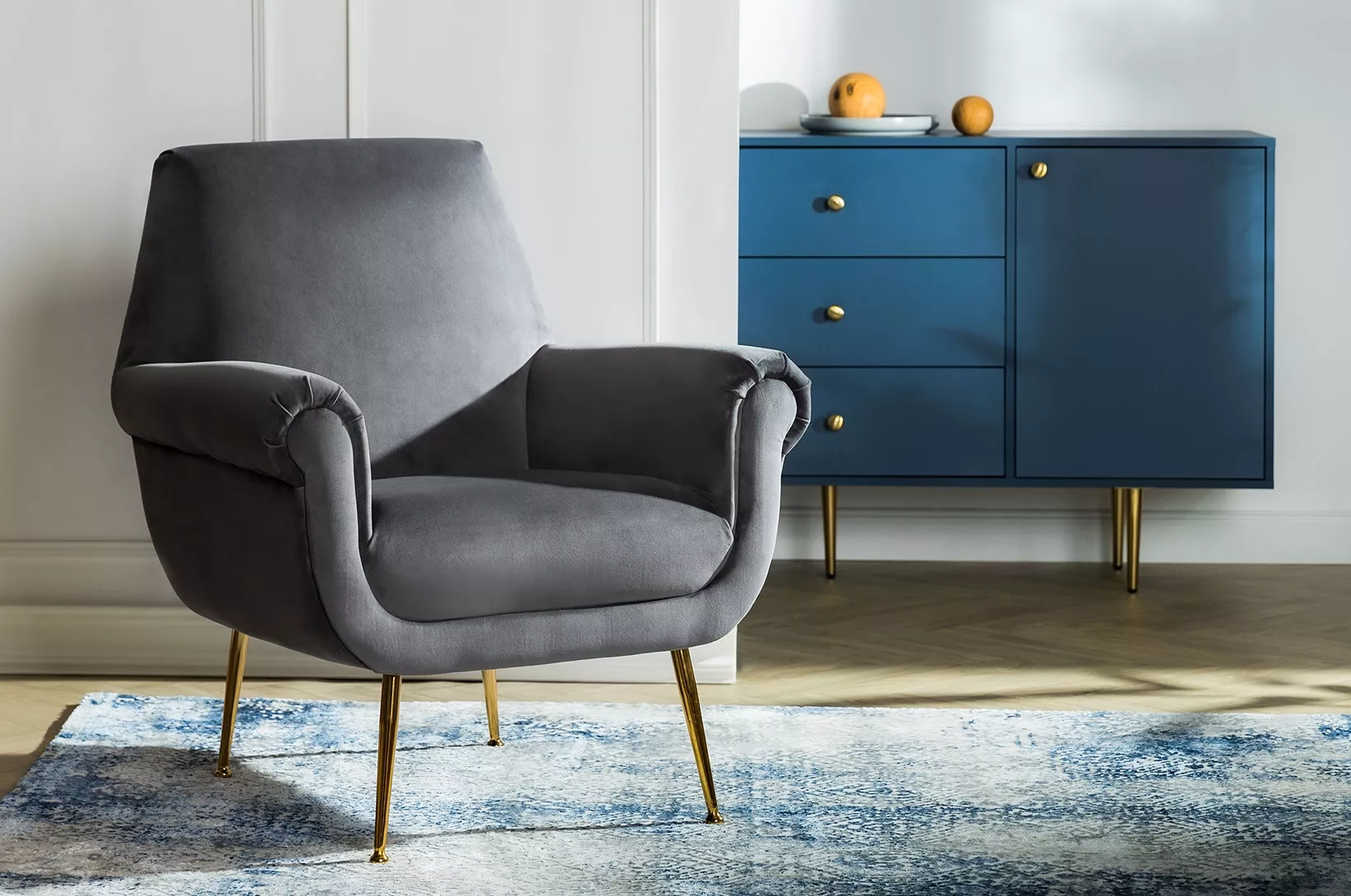 Elegancki fotel do salonu z miękką tapicerką i designerską komodą w tle.
