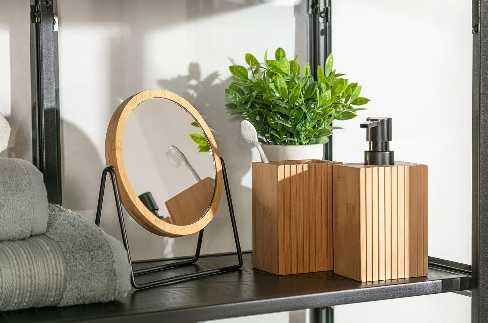 Drewniane akcesoria łazienkowe z lusterkiem, dozownikiem na mydło, pojemnikiem na szczoteczki oraz rośliną dekoracyjną na półce w nowoczesnej łazience.