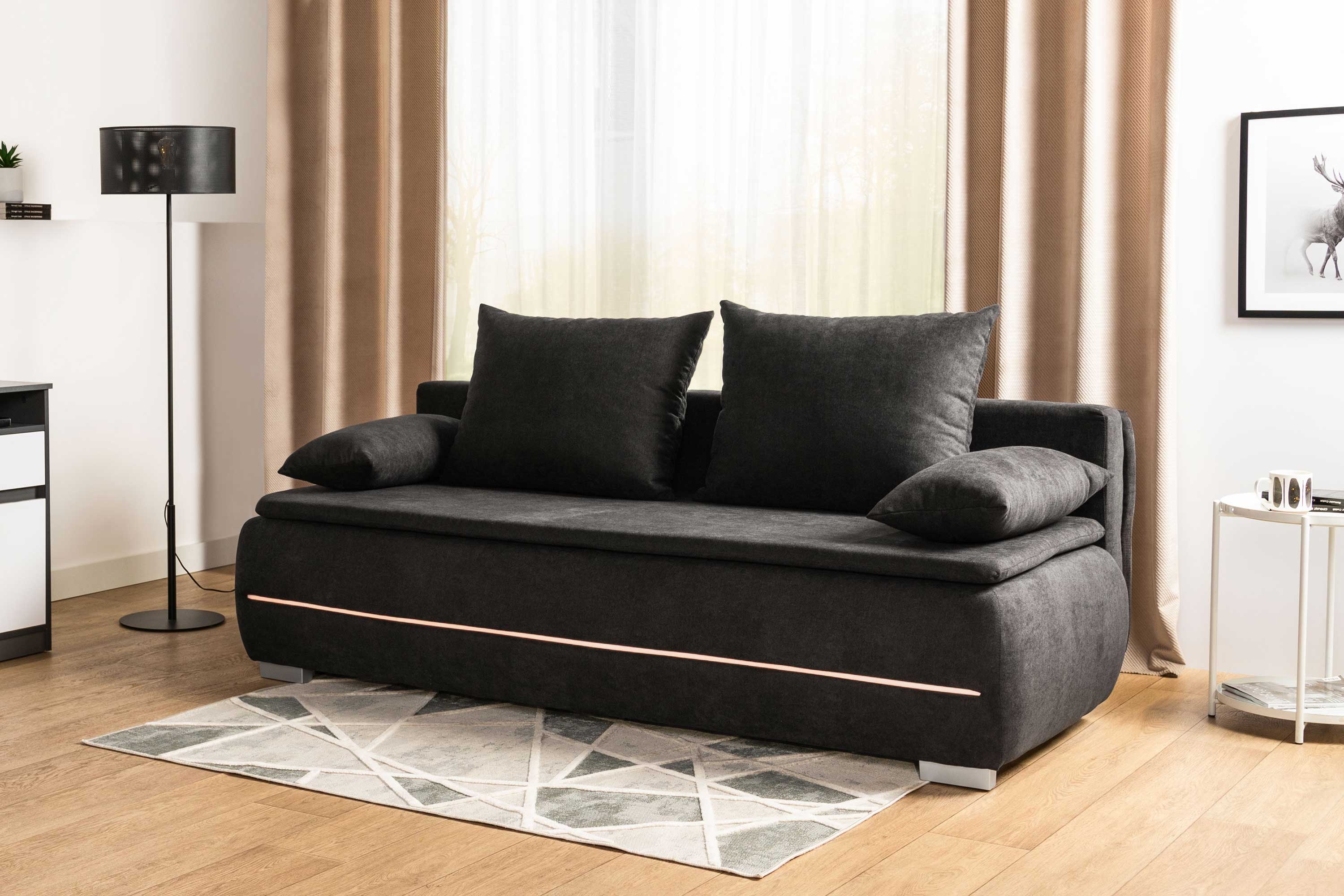 Czarna sofa z funkcją spania i dużymi poduszkami oparciowymi w nowoczesnym salonie, wyposażona w dekoracyjne podświetlenie LED oraz minimalistyczne dodatki.