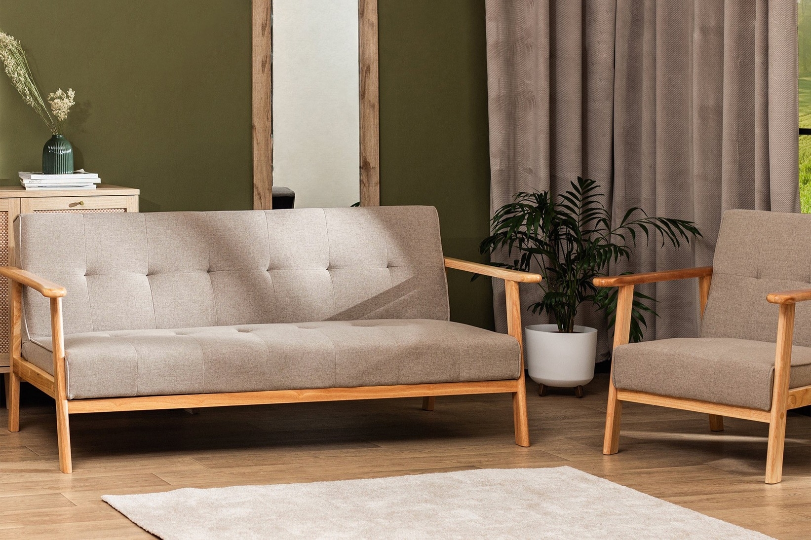 Nowoczesny salon z beżową sofą i fotelem na drewnianym stelażu, urządzony w stylu skandynawskim z zieloną ścianą, roślinami oraz naturalnymi dodatkami.