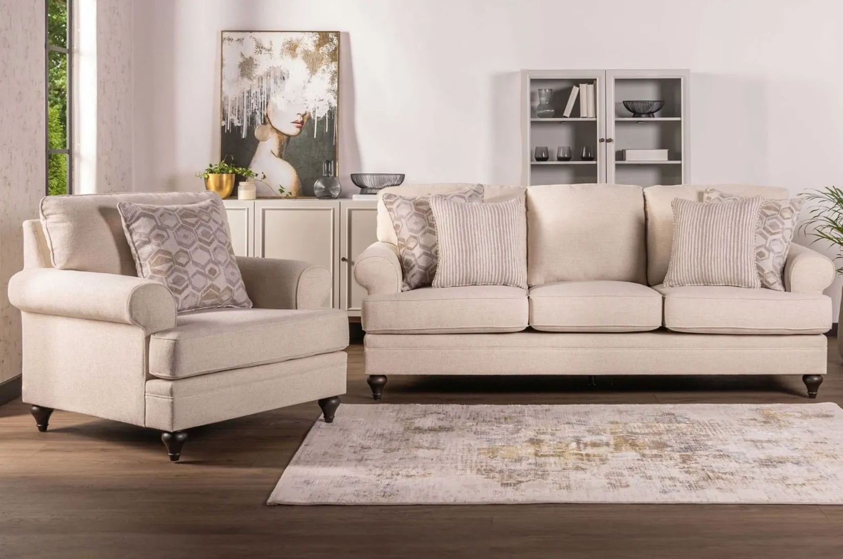 Beżowa sofa i fotel tapicerowany w eleganckim salonie z jasnymi meblami, dekoracyjnymi poduszkami oraz nowoczesnymi dodatkami.