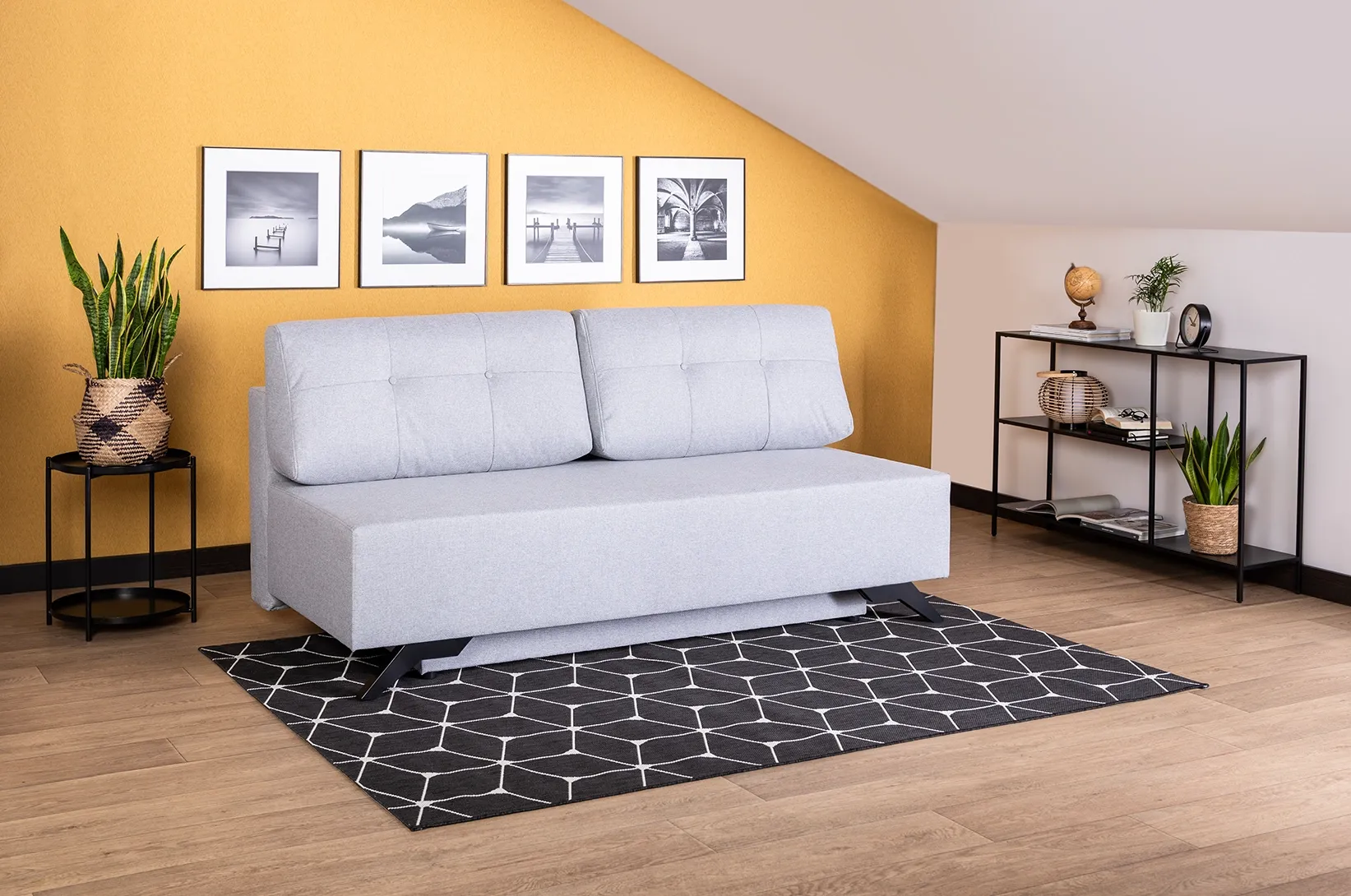 Szara sofa rozkładana z funkcją spania w nowoczesnym salonie z musztardową ścianą, regałem i dekoracjami ściennymi.