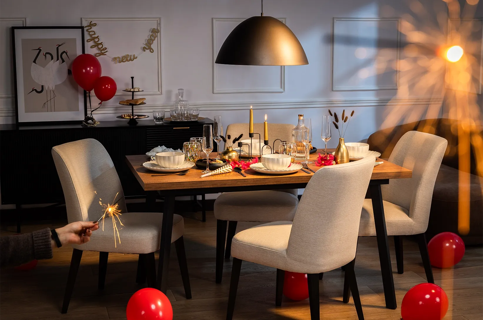 Sylwestrowo udekorowany stół w jadalni z tapicerowanymi krzesłami, świecami, kieliszkami, czerwonymi balonami i zimnymi ogniami w eleganckiej aranżacji wnętrza.