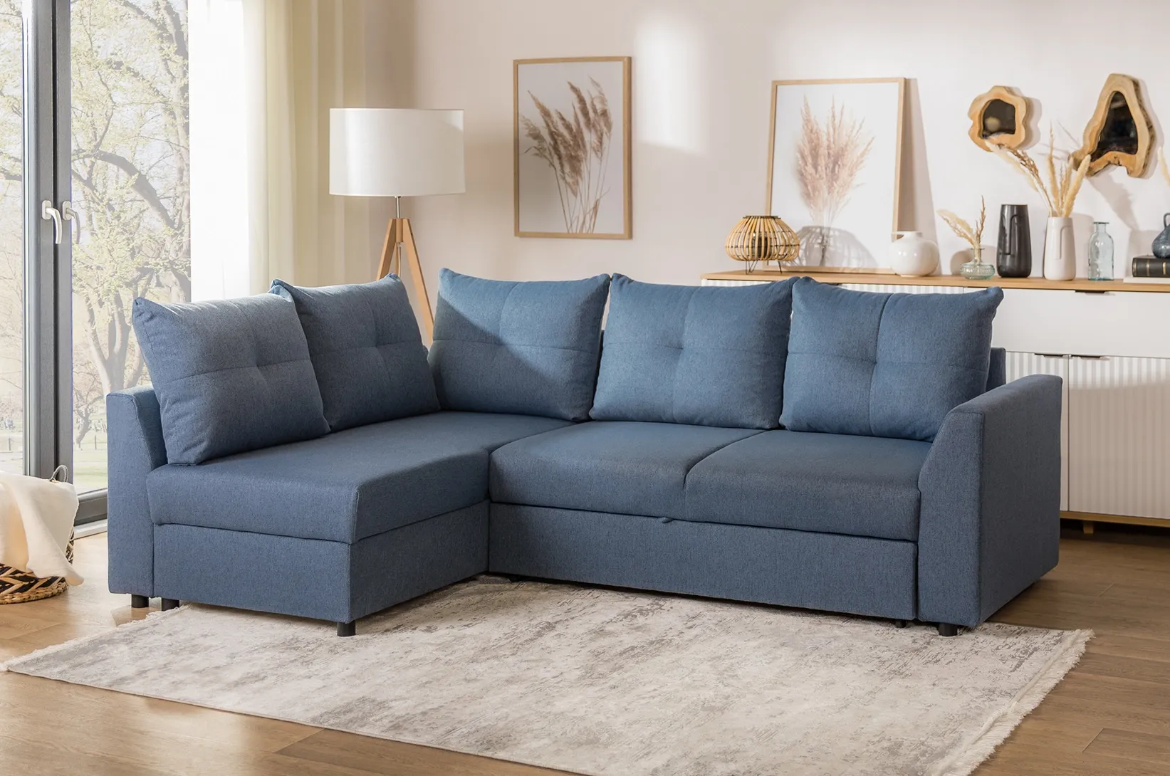 Niebieski narożnik z funkcją spania w nowoczesnym salonie, tapicerowana sofa z dużymi poduszkami na jasnym dywanie w przytulnej aranżacji wnętrza.
