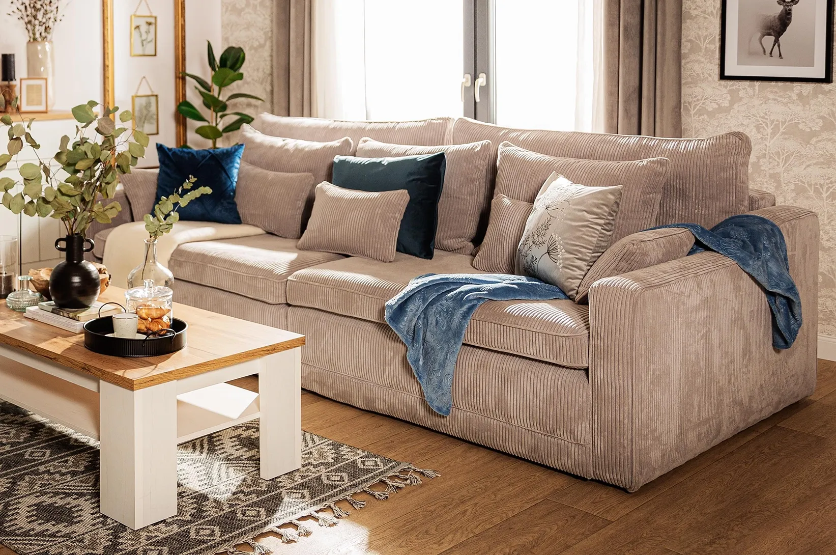 Beżowa sofa sztruksowa z dekoracyjnymi poduszkami i drewnianym stolikiem kawowym, przytulna aranżacja salonu w jasnych, naturalnych kolorach.