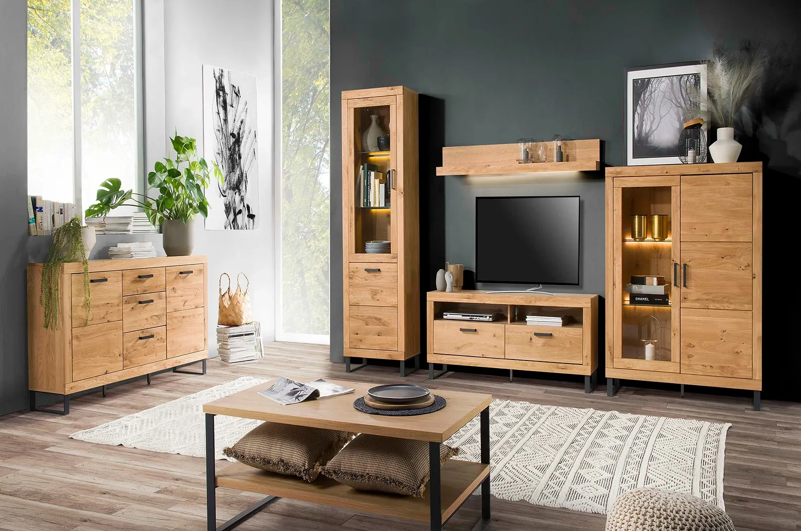 Meble do salonu w kolorze naturalnego drewna z przeszkleniami i czarnymi detalami, w skład których wchodzą komoda, witryna, szafka RTV oraz stolik kawowy.