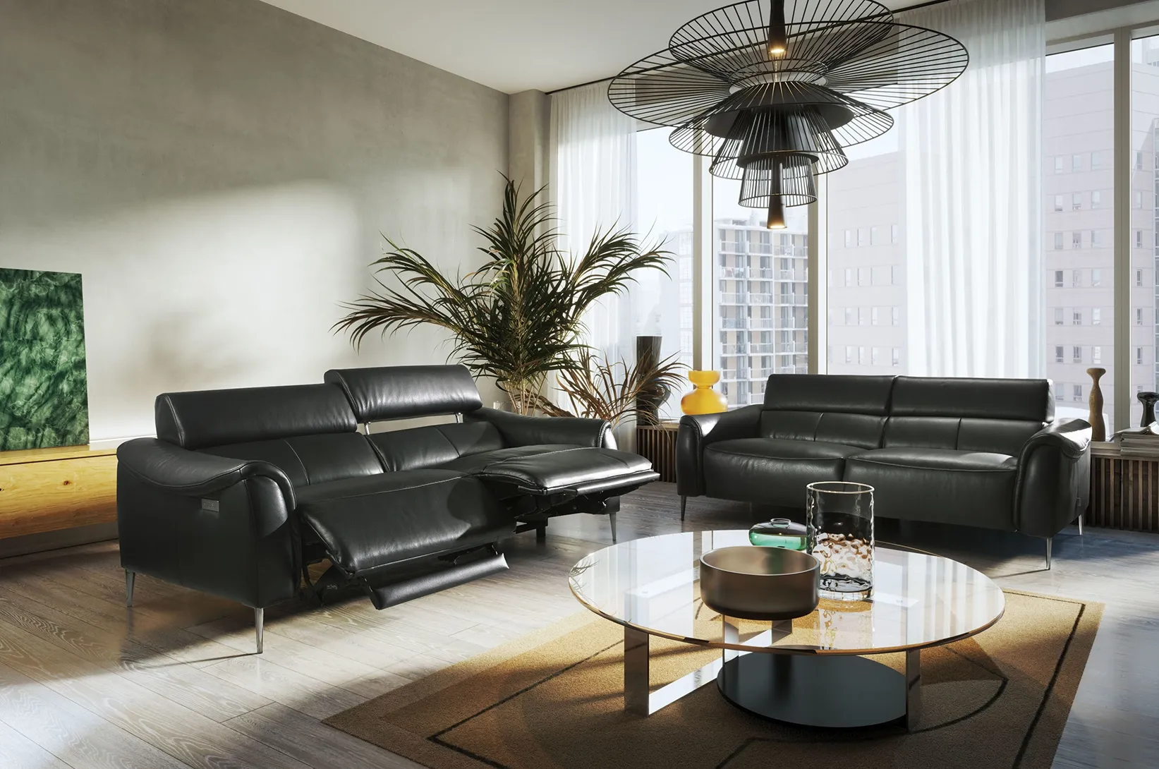 Nowoczesny salon z czarnymi skórzanymi sofami z funkcją relaks, okrągłym stolikiem kawowym oraz dużymi przeszkleniami w eleganckiej aranżacji wnętrza.