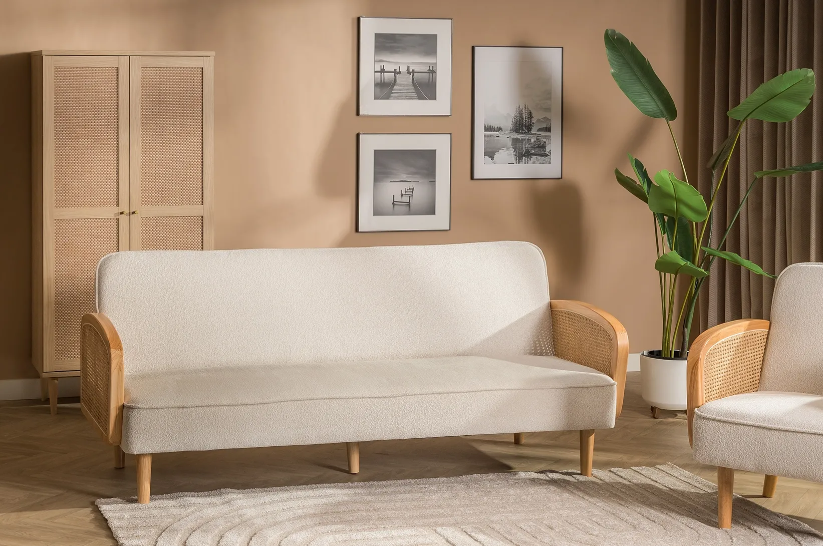 Kremowa sofa do salonu z drewnianymi podłokietnikami i plecionymi bokami, ustawiona obok fotela i szafy w naturalnej aranżacji wnętrza.