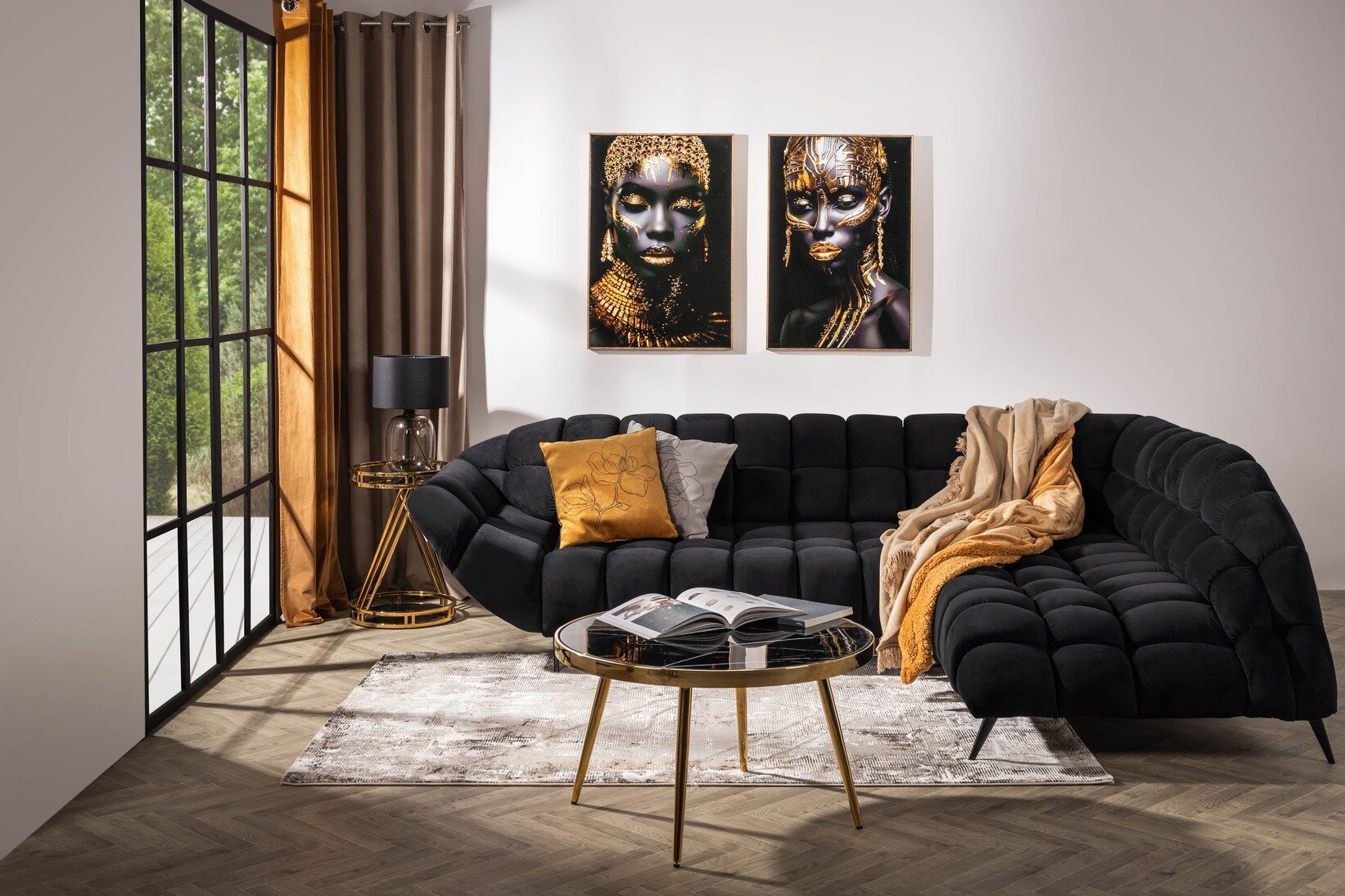 Czarna sofa narożna z pikowanym siedziskiem oraz złotymi akcentami, ustawiona w eleganckim salonie z okrągłym stolikiem kawowym i dekoracyjnymi obrazami w stylu glamour.