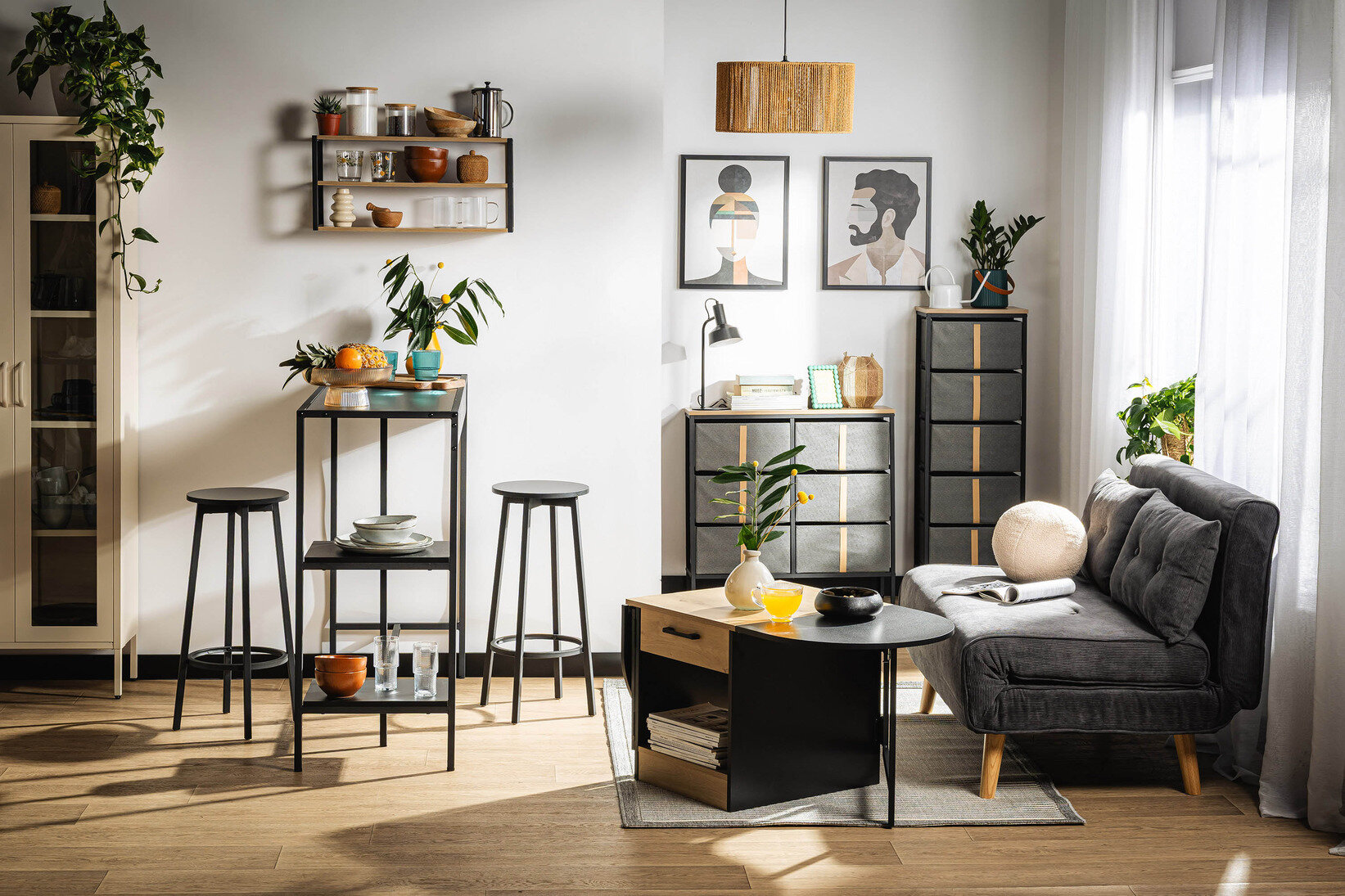 Nowoczesny salon z aneksem jadalnianym w stylu loftowym, szara sofa, drewniany stolik kawowy, czarne regały oraz wisząca lampa nad częścią wypoczynkową.